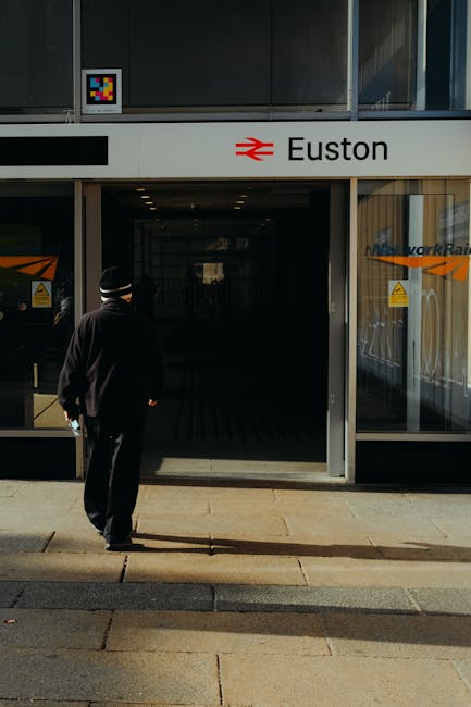 The image shows a section of Euston station in London, with a large black building bearing the station's name 'Euston' in white letters alongside British railway and London Underground symbols. In the